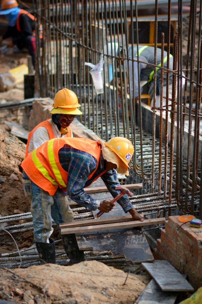 Two workers in yellow helmets and orange vests at rebar